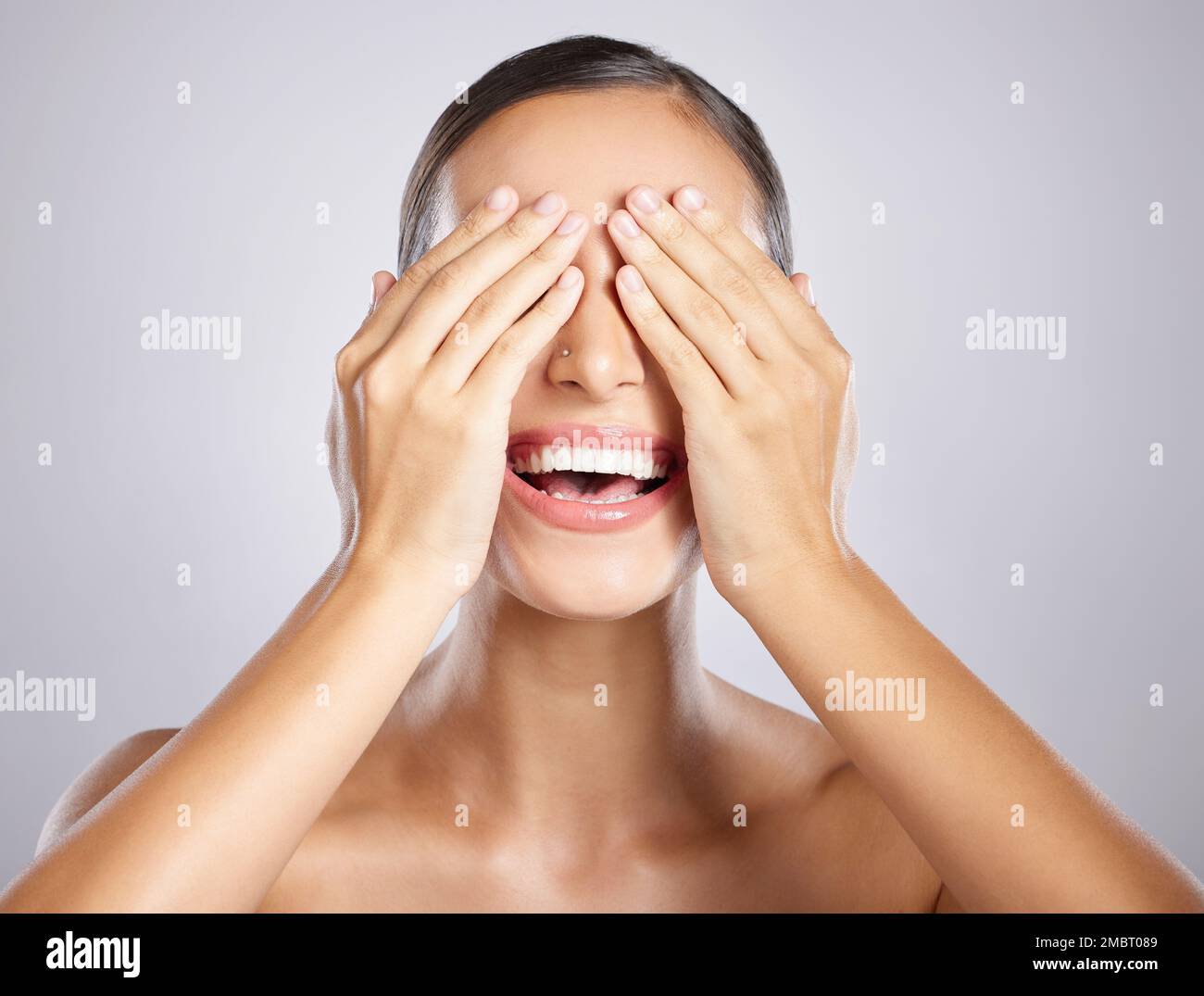 Femme, les mains et les yeux couvrant avec le sourire en satisfaction pour les soins de la peau, les cosmétiques ou la beauté sur un fond gris studio. Modèle féminin heureux Banque D'Images