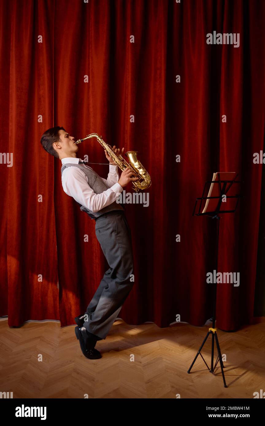 Un jeune musicien joue du saxophone ténor sur scène avec des rideaux drapés rouges Banque D'Images