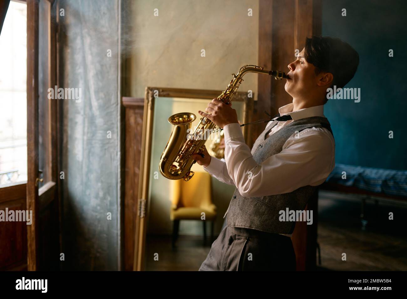 Jeune homme élégant jouant du saxophone alto d'or dans la salle de brumisation Banque D'Images