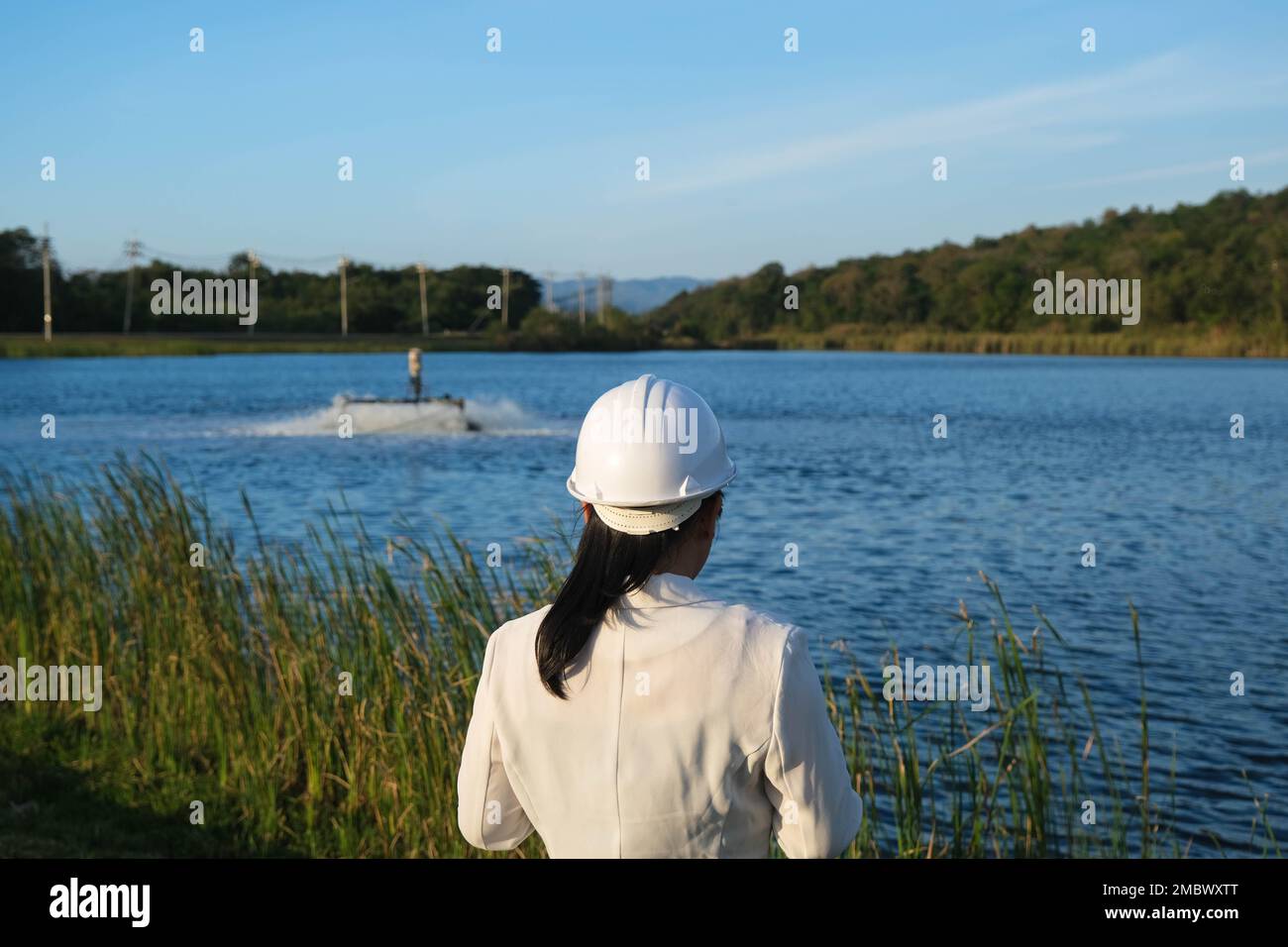 Un ingénieur de l'environnement portant un casque blanc utilise un téléphone portable pour faire fonctionner un aérateur à turbine à oxygène dans un étang. Concept de l'eau et de l'écologie. Banque D'Images