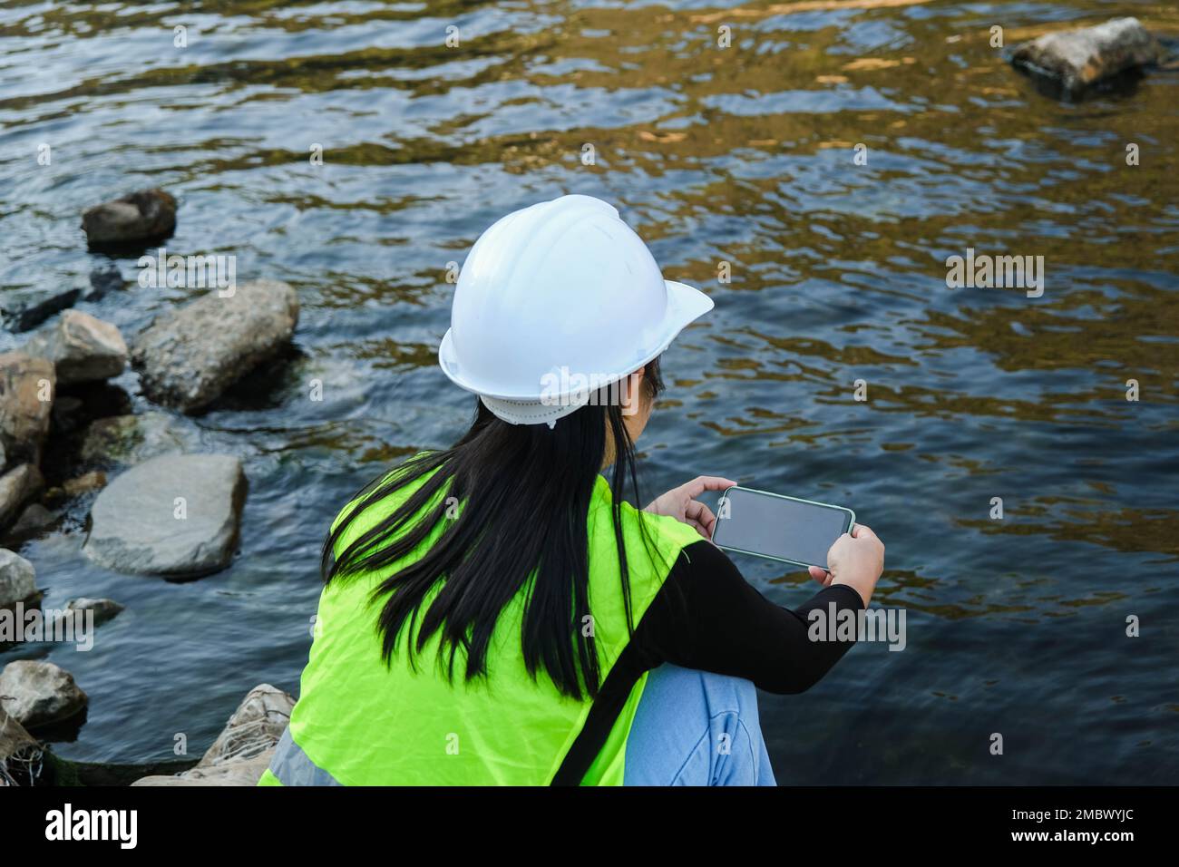 L'ingénieur en environnement utilise un téléphone portable pour enregistrer les données d'analyse de l'eau dans le barrage. Les écologistes collectent des échantillons d'eau du barrage pour vérifier la présence de con Banque D'Images