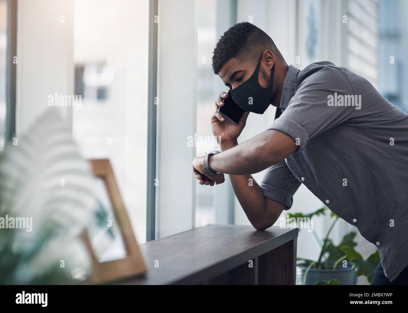 Quand puis-je m'attendre à une mise à jour. un jeune homme d'affaires portant un masque facial et vérifiant le temps tout en parlant sur un téléphone portable dans un bureau. Banque D'Images