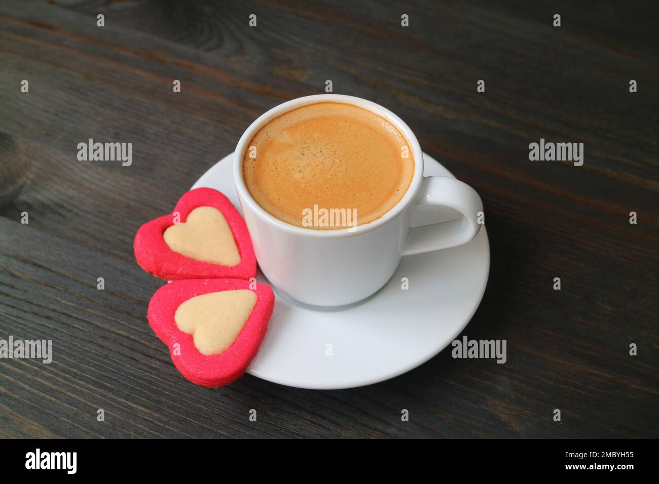 Tasse de café expresso avec une paire de biscuits en forme de cœur sur fond en bois noir Banque D'Images