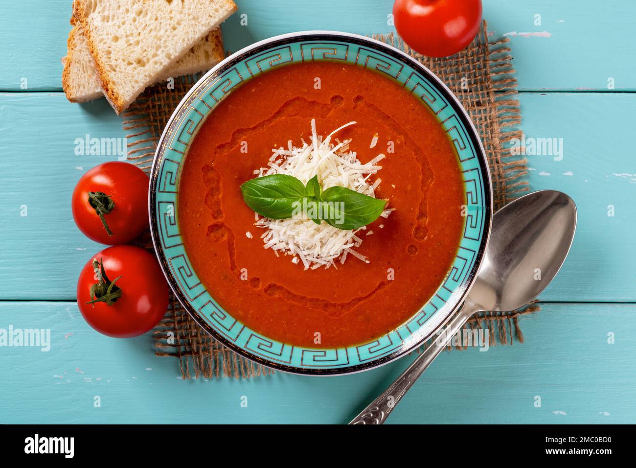 Bol de soupe de tomates maison sur table en bois turquoise. Purée italienne de tomates rôties au parmesan et au basilic. Savoureux plat végétarien. Banque D'Images