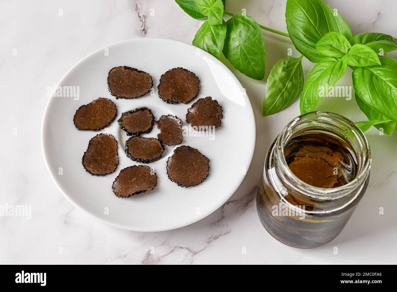 Tranché de truffe noire sur une assiette et bocal de carpaccio de truffe tranches dans l'huile sur fond de marbre. Tuber melanosporum, champignon en conserve. Gourme Banque D'Images