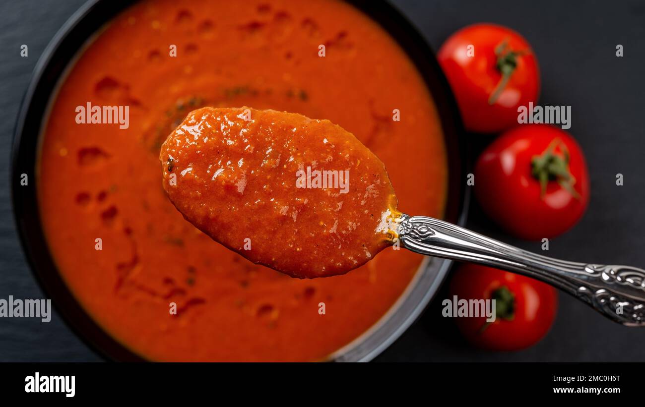 Cuillère de soupe de tomate chaude sur le bol en gros plan. Repas de plat de légumes de tomates rôties en purée, d'ail et de basilic. Plat végétarien sain. Macro. Banque D'Images