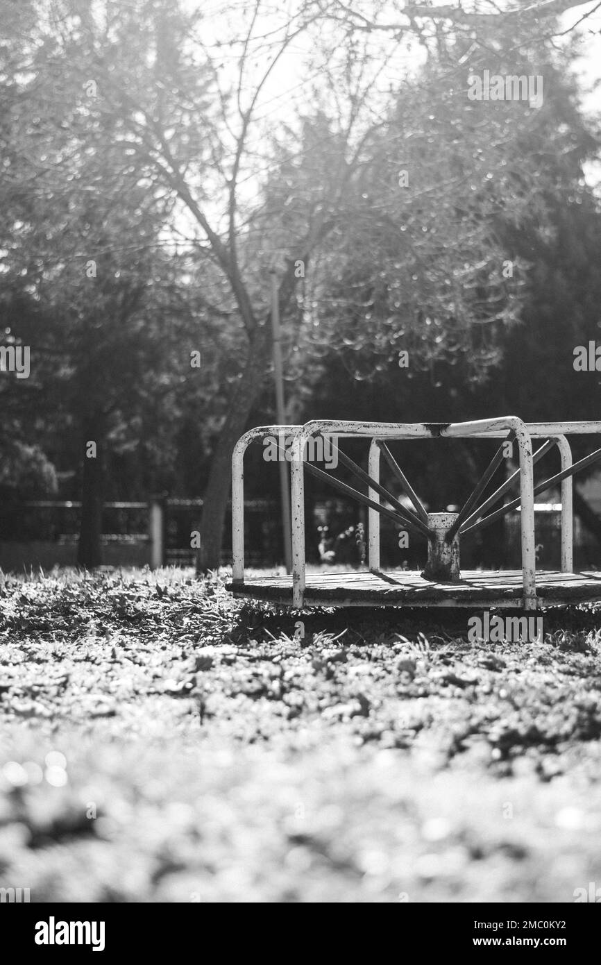 Une échelle de gris verticale d'un vieux terrain de jeu pour les enfants avec un carrousel en métal rouillé Banque D'Images