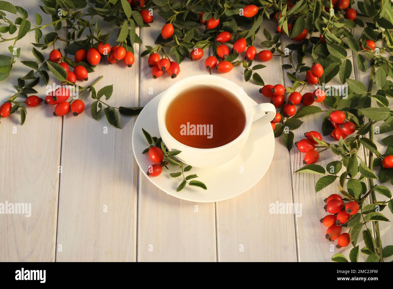 Tasse de thé avec baies de rose sur fond de bois blanc Banque D'Images