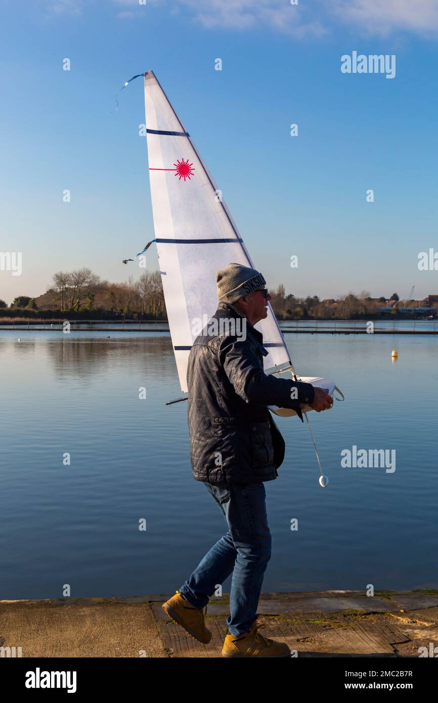 Poole, Dorset Royaume-Uni. 21 janvier 2023. Météo au Royaume-Uni : un matin glacial et froid à Poole ne dissuade pas les passionnés de bateaux radiocommandés de faire des courses sur leurs modèles laser autour du lac Poole Park. Peu de vent et de taches gelées rendent la course difficile, mais créent une scène calme et sereine avec de beaux reflets au soleil. Homme portant son bateau. Crédit : Carolyn Jenkins/Alamy Live News Banque D'Images