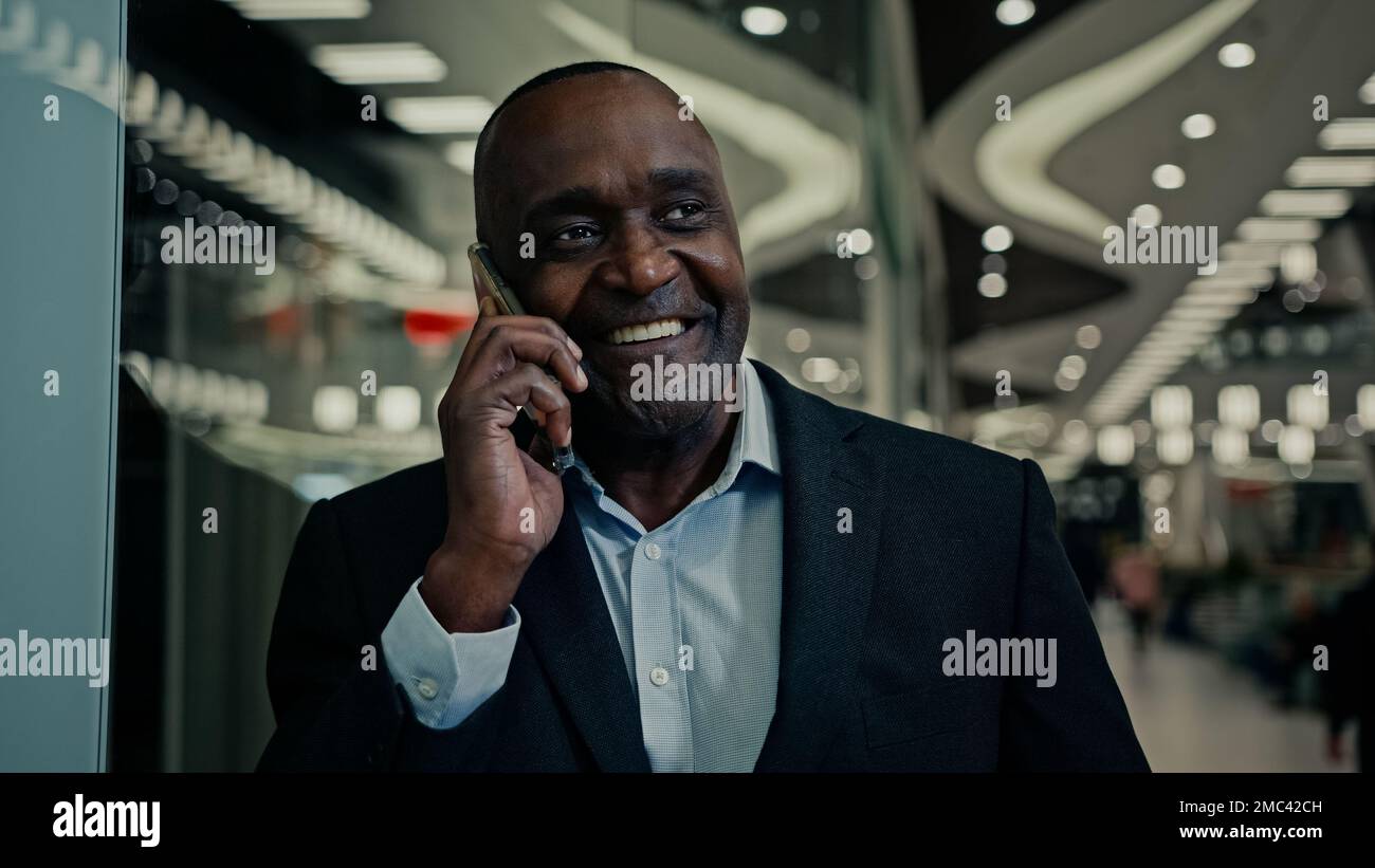 Homme d'affaires ethnique afro-américain souriant d'âge moyen à l'intérieur répondre à un appel écouter de bonnes nouvelles téléphone mobile appeler parler victoire Banque D'Images