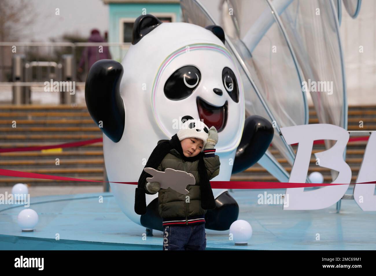 A child wearing a panda hat stands near Bing Dwen Dwen, the mascot for the 2022 Winter Olympics, outside a park in Beijing on Thursday, Feb. 17, 2022. The Olympics returned this year to a China that has changed in many ways, and the atmosphere has been much more subdued. (AP Photo/Ng Han Guan) Banque D'Images