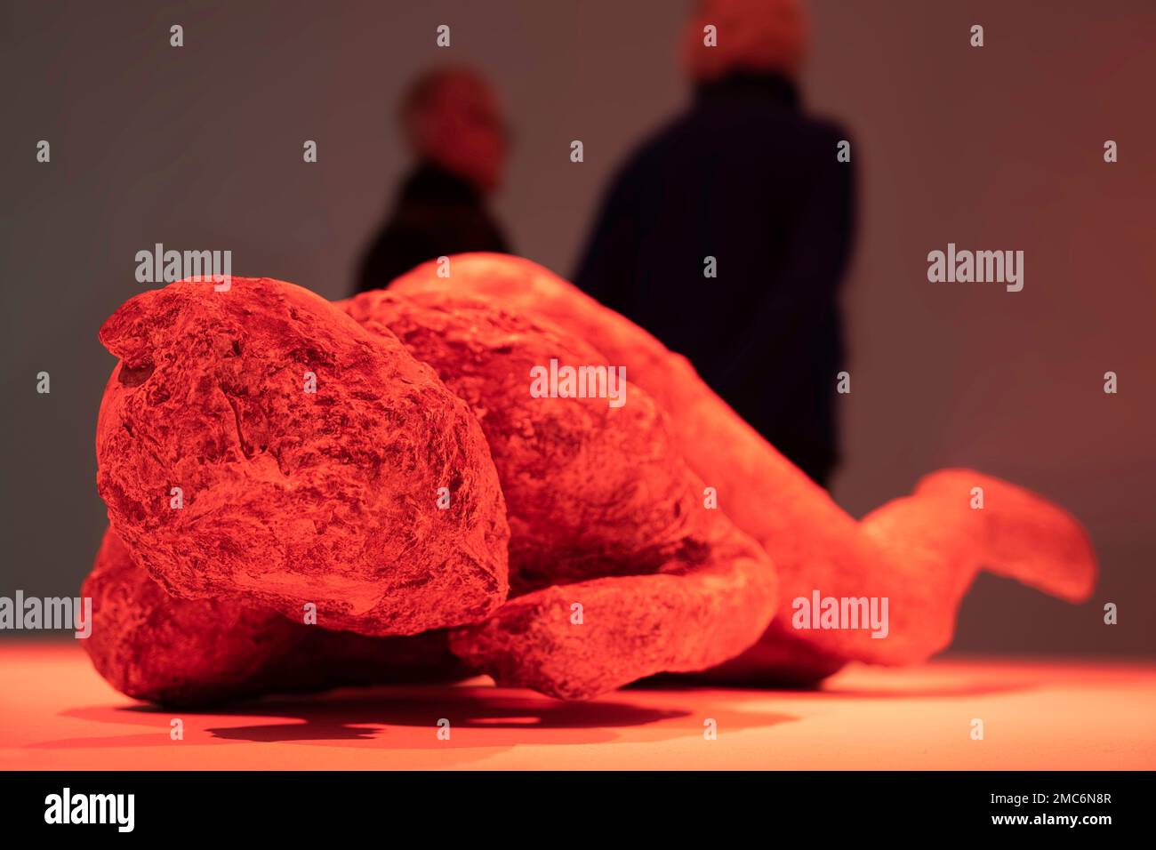 Couple dans un musée derrière une coulée de plâtre d'une victime allongée, trouvée à Pompéi, illuminée de feux rouges pour suggérer l'éruption du volcan Banque D'Images