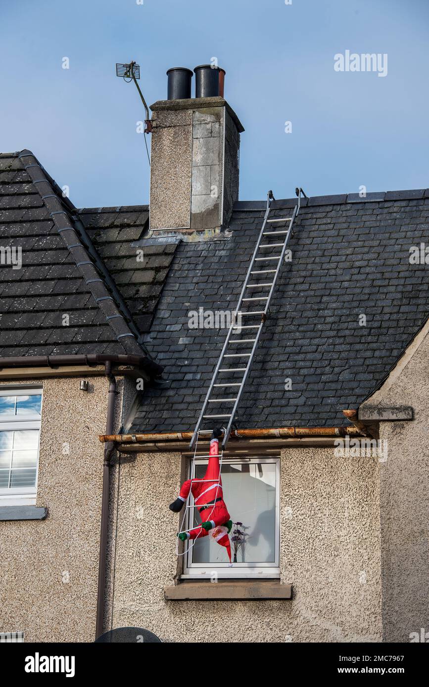 Santa Calause tombant des laddders sur le toit de la maison le jour de Noël. Banque D'Images