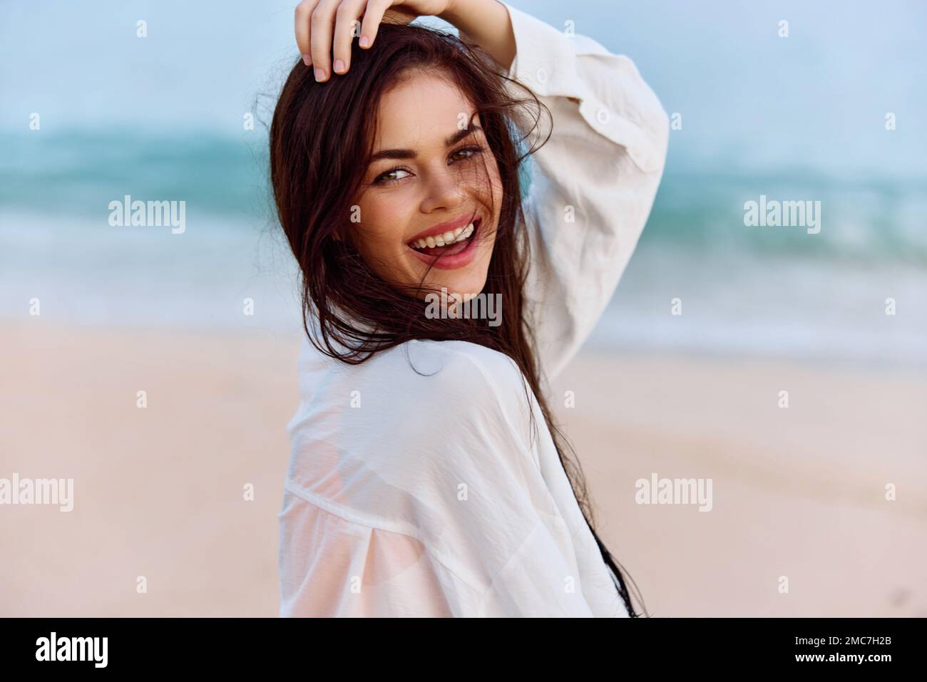 Portrait d'une femme souriant avec des dents avec une peau bronzée dans un débardeur jaune et une chemise de plage blanche avec des cheveux mouillés après avoir nagé sur la plage de l'océan Banque D'Images