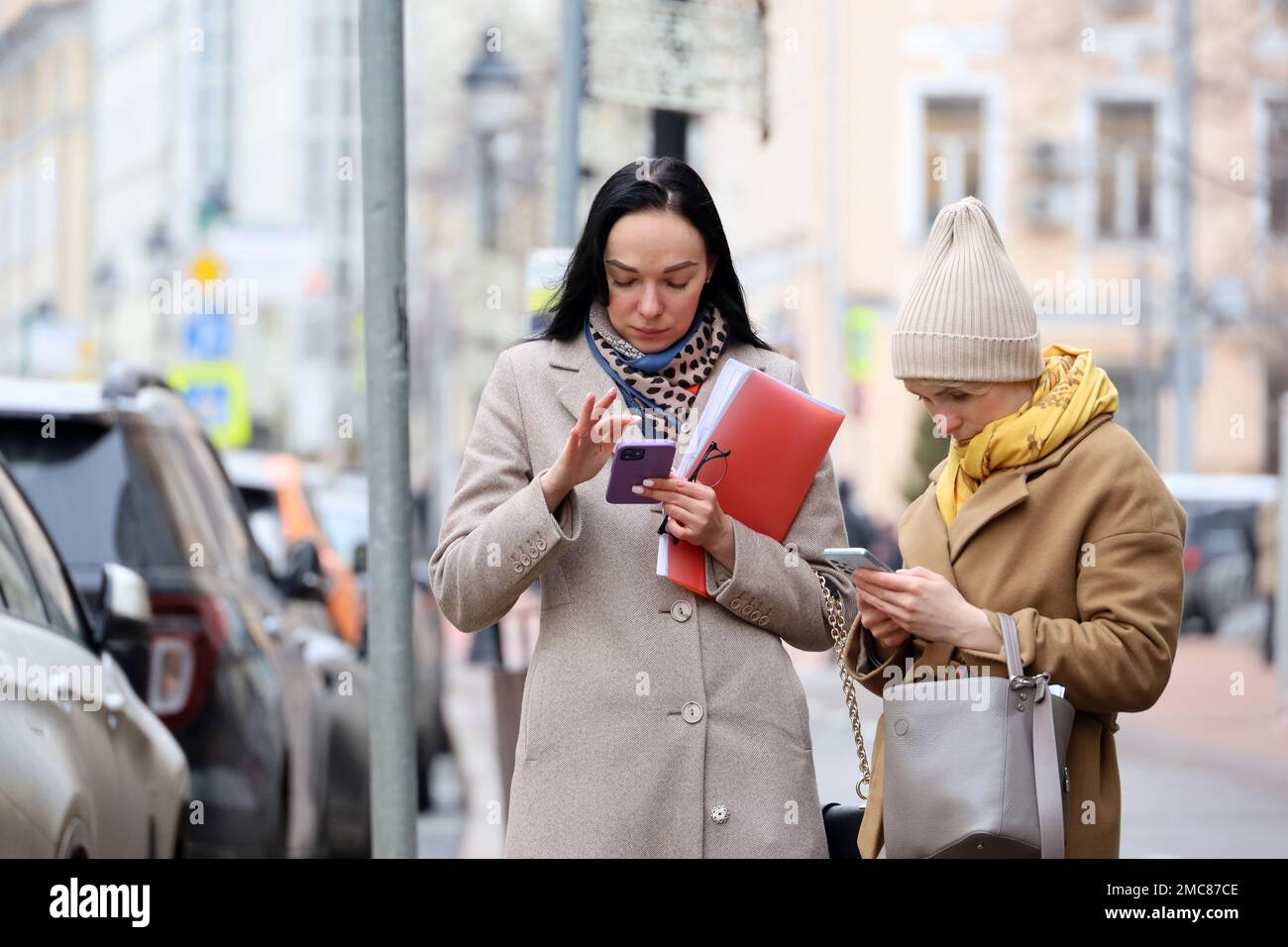 Personnes utilisant un smartphone dans la rue urbaine. Deux jeunes femmes dans des vêtements chauds avec des téléphones portables dans les mains Banque D'Images