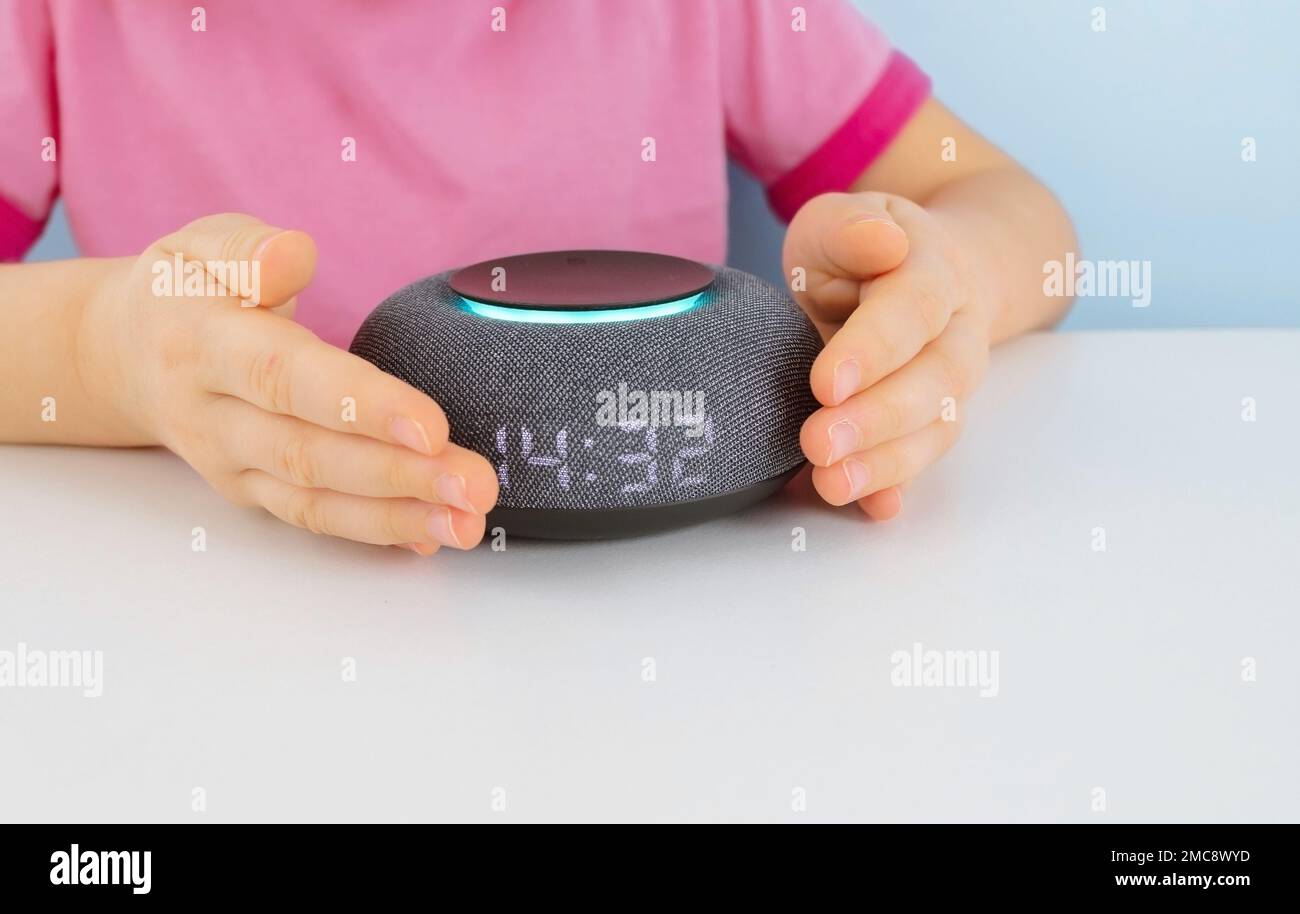 Petit enfant utilisant une enceinte intelligente à la maison pendant ses devoirs. Petite fille qui parle avec un haut-parleur intelligent et lui donne des ordres Banque D'Images