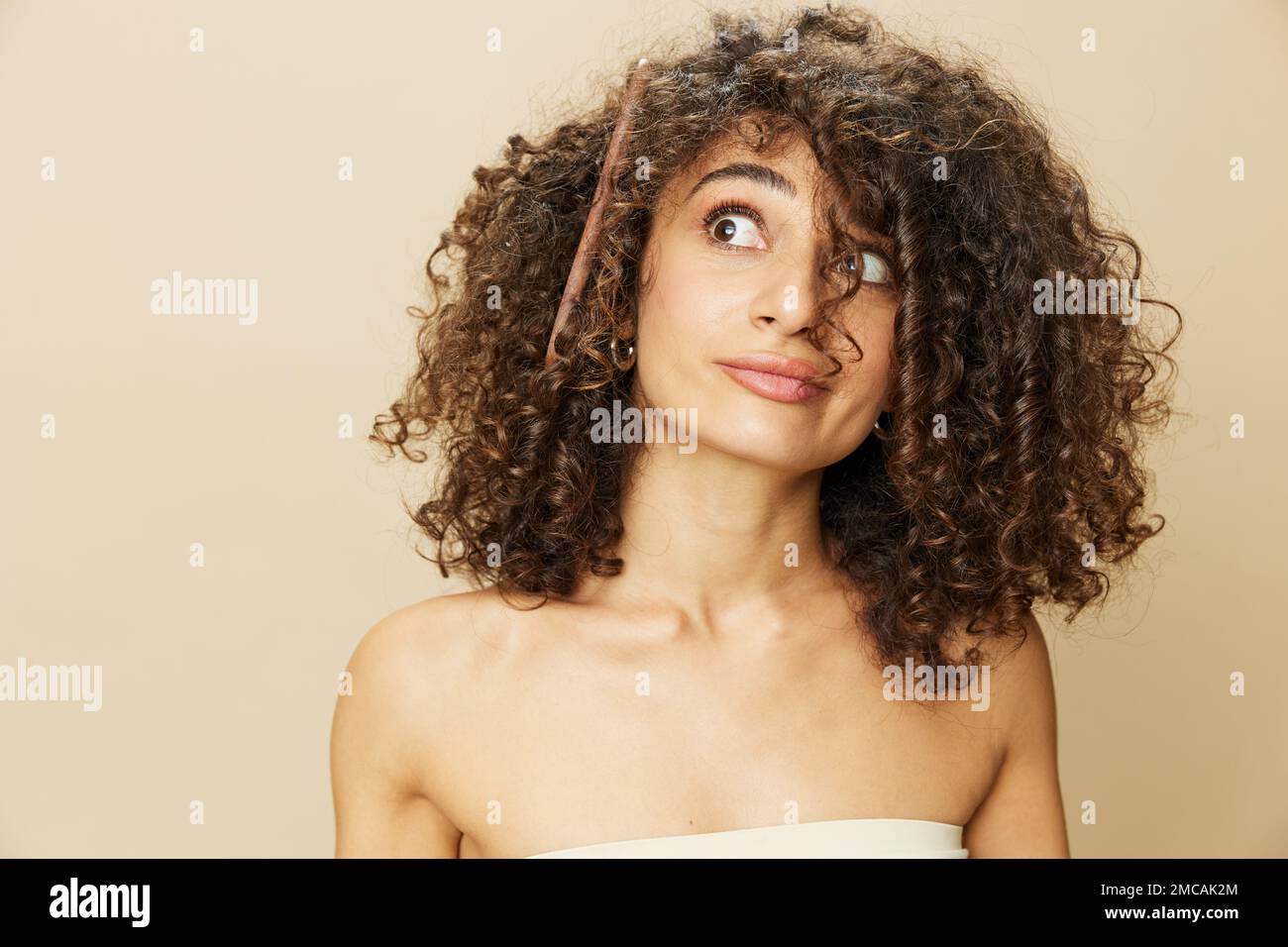 Femme peigne les cheveux bouclés afro avec peigne en bois, produits de coiffage de soins de beauté maison, perte de cheveux après Covid-19, sourire sur fond beige Banque D'Images