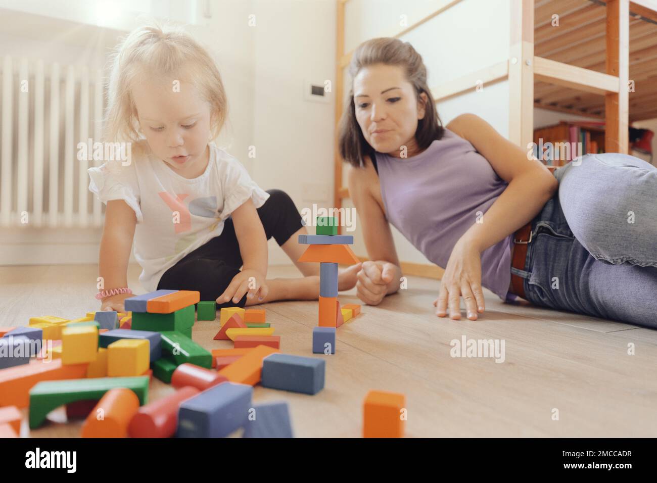 Dans une pièce lumineuse et colorée, mère et fille jouent avec des constructions en bois colorées, parlant les uns aux autres comme ils construisent et inventent Banque D'Images