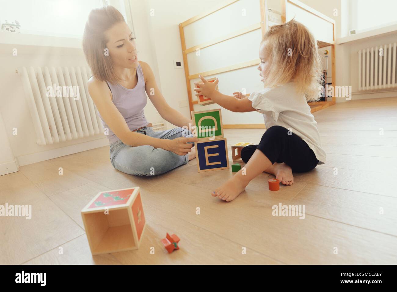 la mère et la fille jouent avec des cubes en bois, avec des lettres sur les visages et capable de contenir des plus petits; la pièce est claire et claire Banque D'Images
