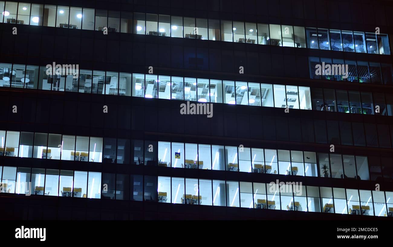 Immeuble de bureaux moderne dans la ville la nuit. Vue sur les bureaux éclairés d'un bâtiment d'entreprise. Voyant clignotant dans la fenêtre de la construction de plusieurs étages Banque D'Images