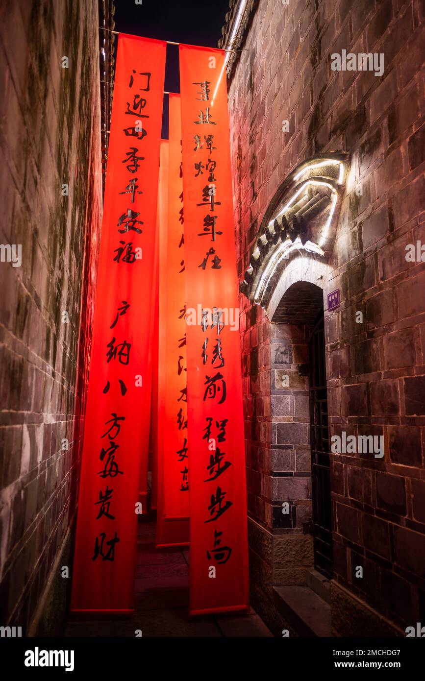 Bannières rouges avec script chinois accrochées dans une rue étroite la nuit Banque D'Images