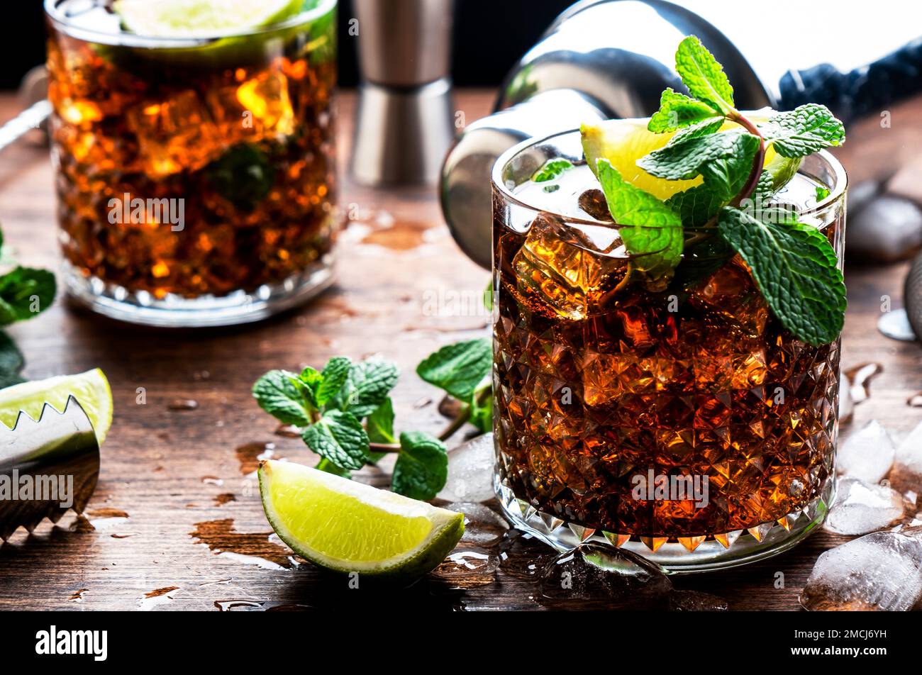 Cocktail au rhum cola avec alcool fort et glace, garni de menthe et de lime  en verre. Fond en bois, lumière dure Photo Stock - Alamy