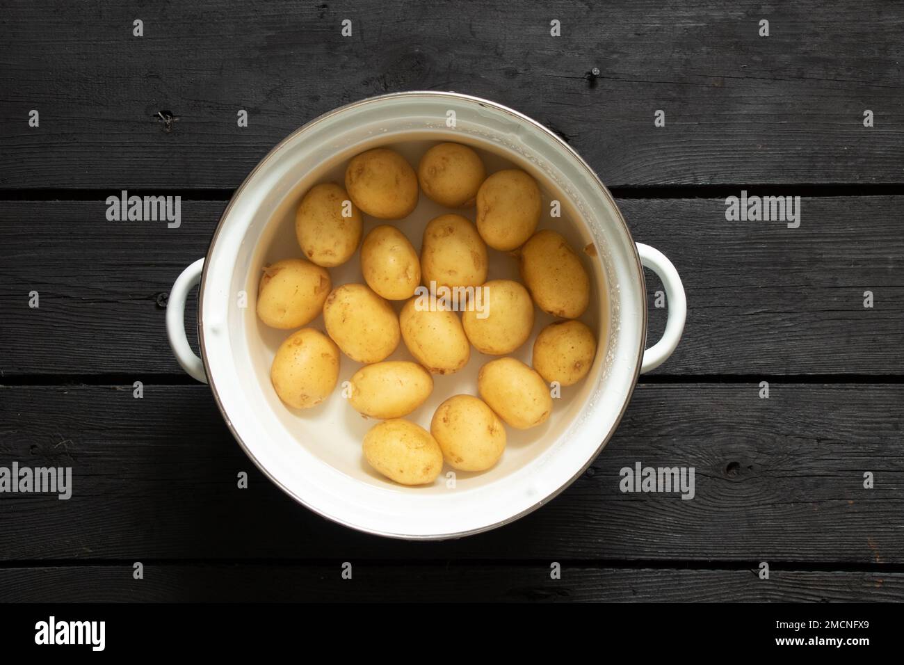 les jeunes pommes de terre brutes entières dans l'eau dans une casserole sont sur une table en bois noir, les pommes de terre dans une casserole, les faire bouillir Banque D'Images