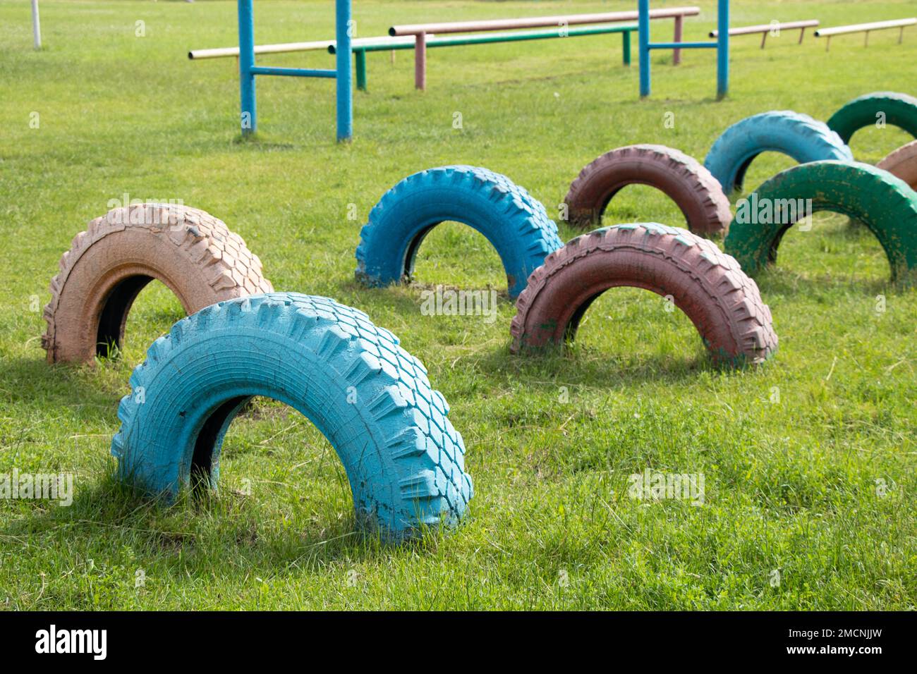 les vieux pneus peints avec de la peinture sont enterrés dans le sol sur le terrain de jeux pour enfants pour la fixation, les pneus sont dans le sol sur la pelouse Banque D'Images