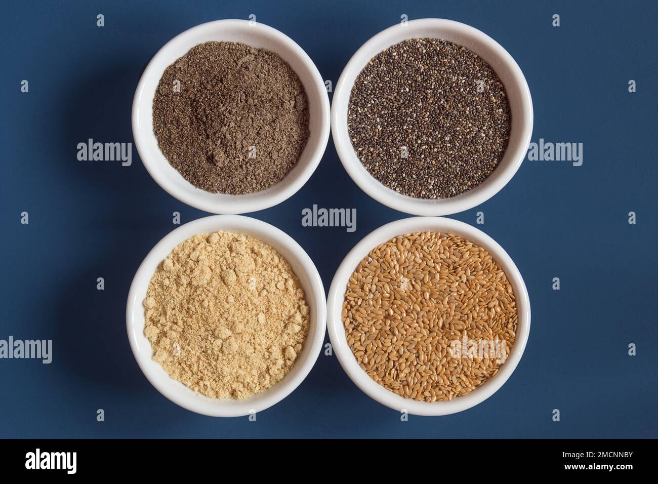 Vue de dessus de 4 bols de nourriture remplis de chia et de lin à la fois moulu et entier sur un fond bleu. Graines et nourriture. Banque D'Images
