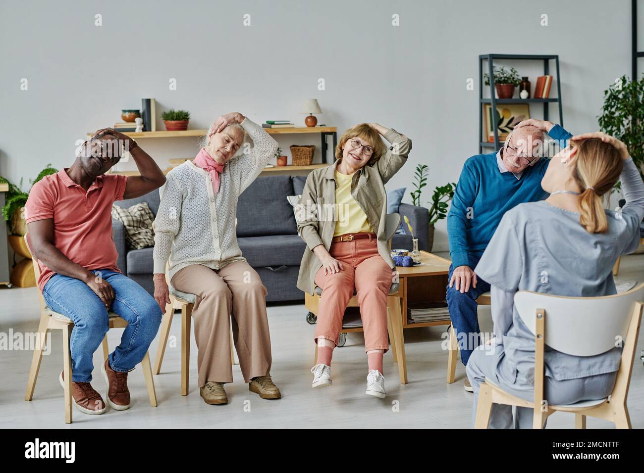 Groupe de personnes âgées assises sur des chaises et faisant des exercices physiques avec un instructeur Banque D'Images
