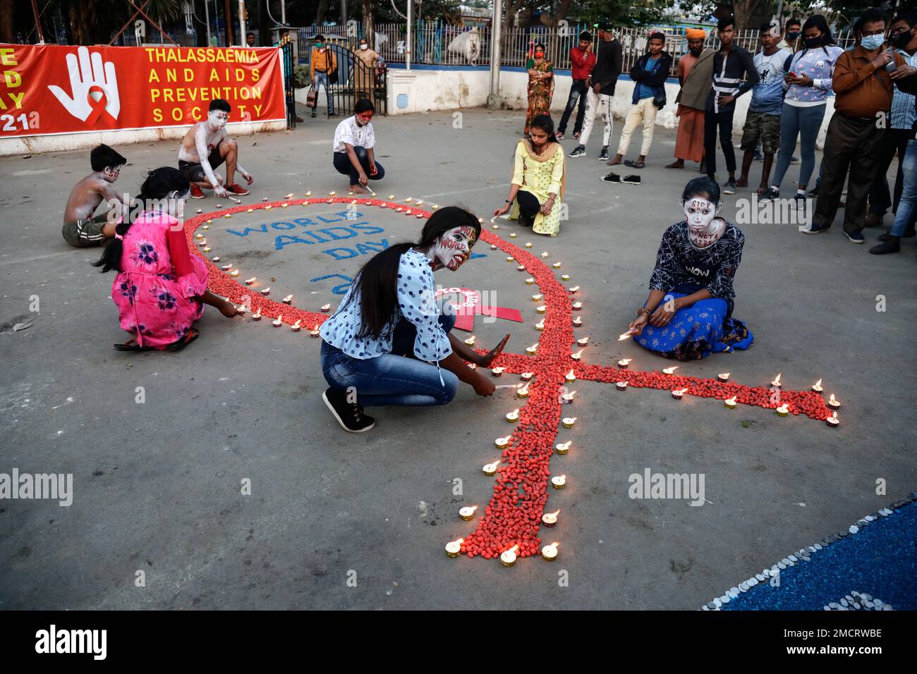 People light candles in the formation of a red ribbon, the universal symbol of awareness and support for those living with HIV, on World AIDS Day in Kolkata, India, Wednesday, Dec. 1, 2021. (AP Photo/Bikas Das) Banque D'Images