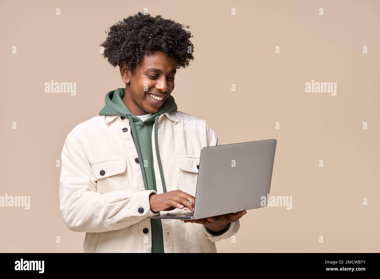 Un étudiant afro-américain souriant utilisant un ordinateur portable isolé sur fond beige. Banque D'Images