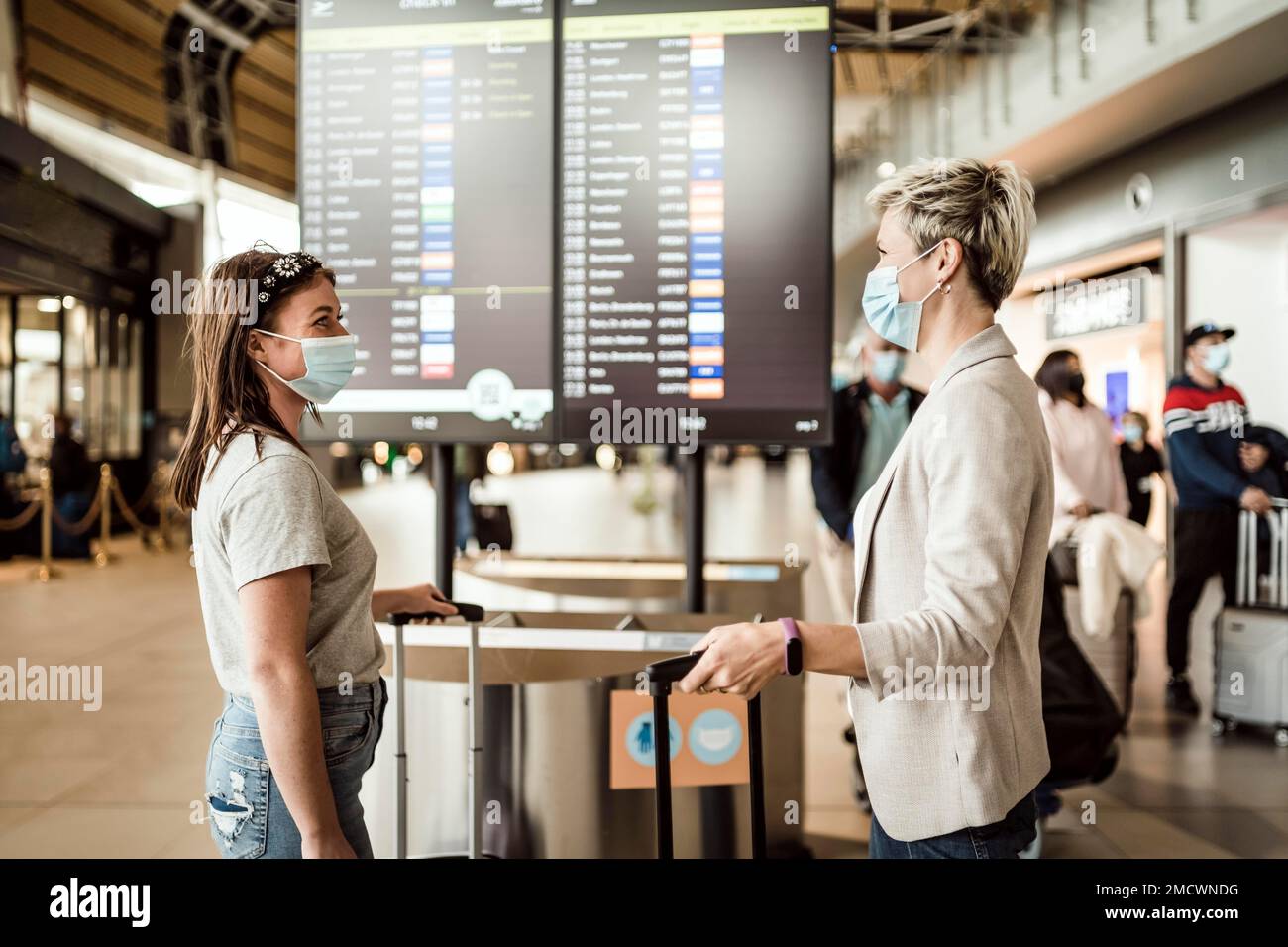 Deux femmes voyageant portant des masques de protection discutant à l'aéroport de Faro par le conseil d'information de vol Banque D'Images