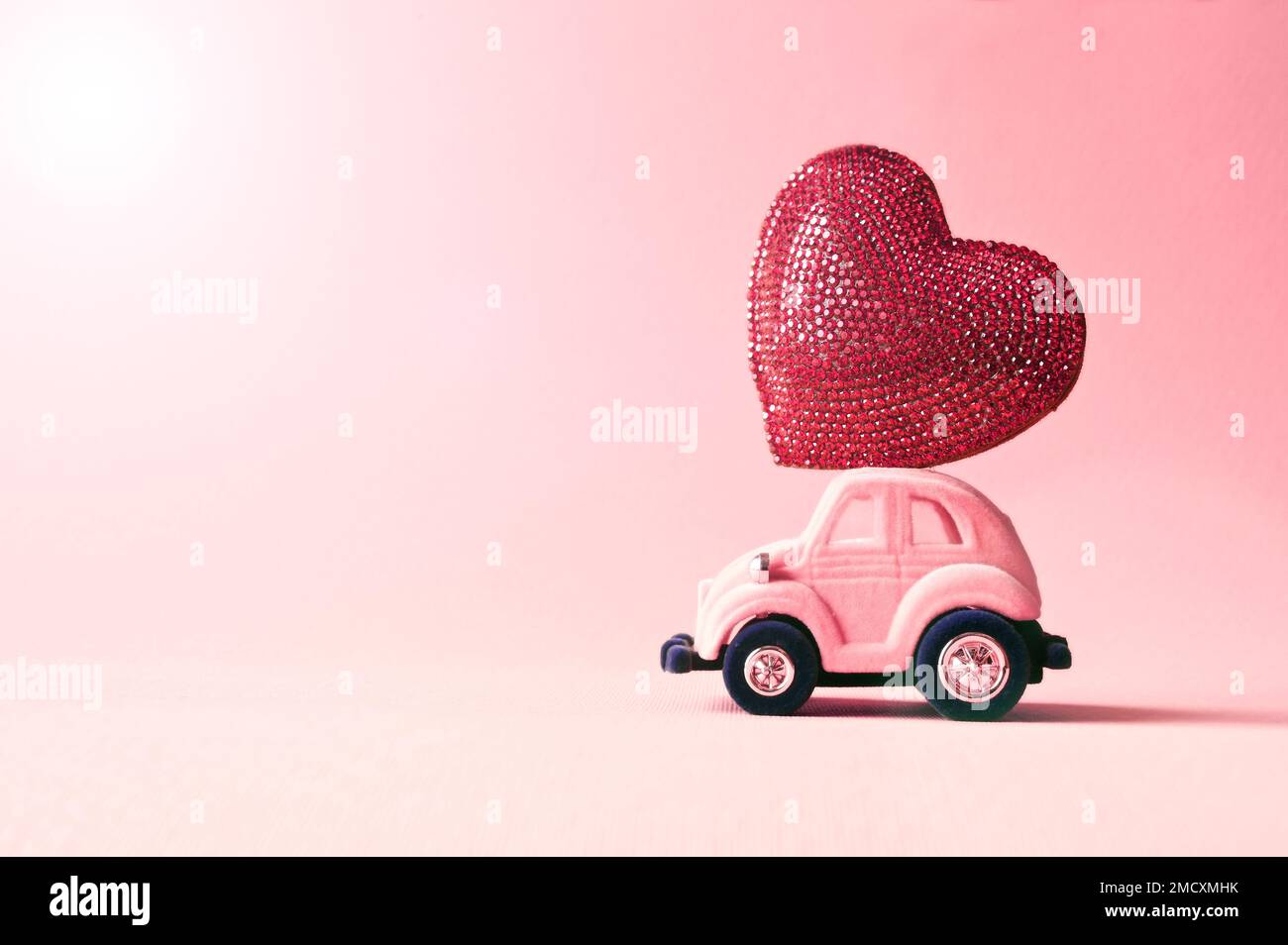 Voiture-jouet rétro offrant un coeur d'artisanat pour la Saint-Valentin sur fond rose Banque D'Images