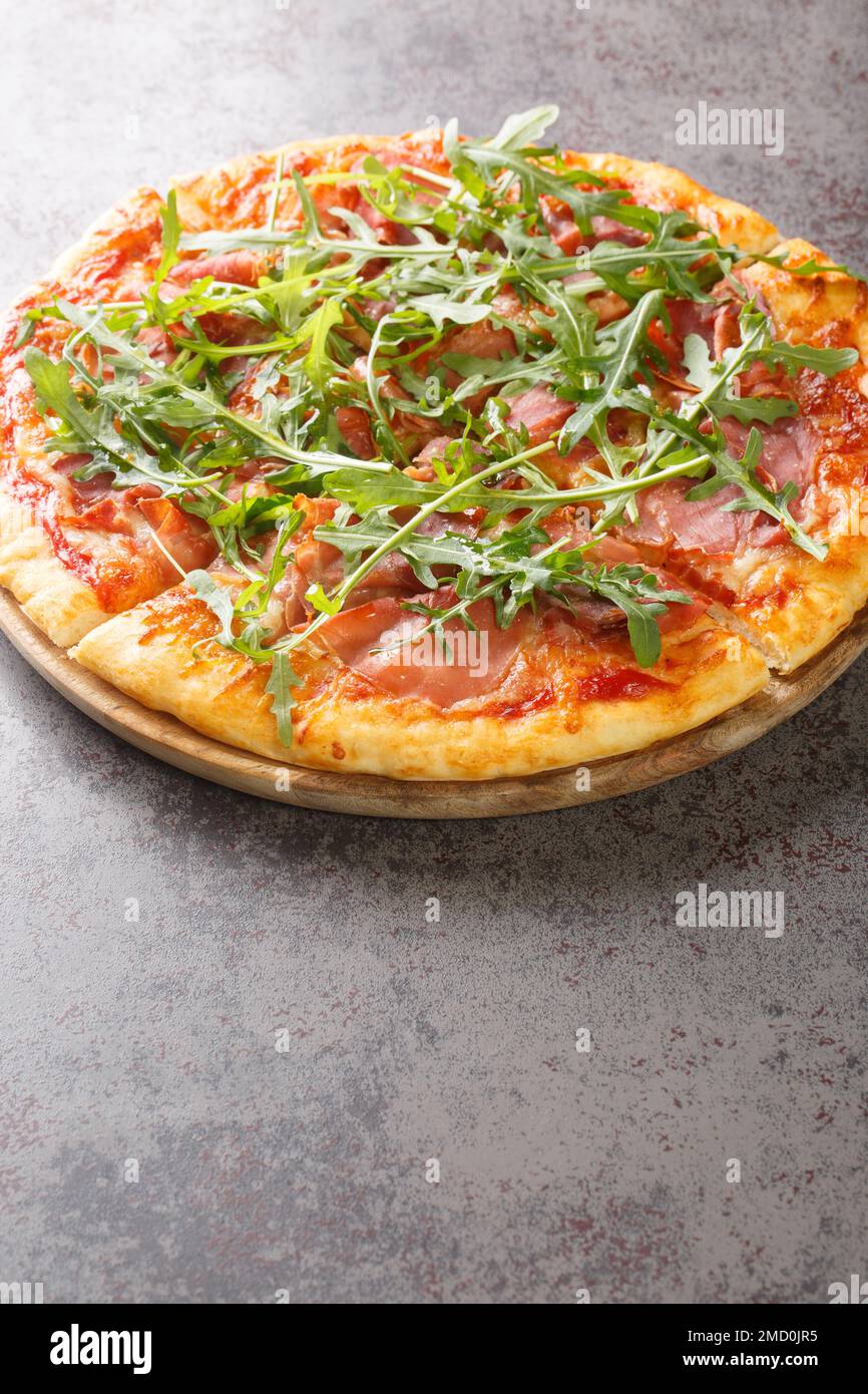 Pizza prosciutto au fromage, sauce tomate et roquette fraîche sur une planche de bois sur la table. Verticale Banque D'Images