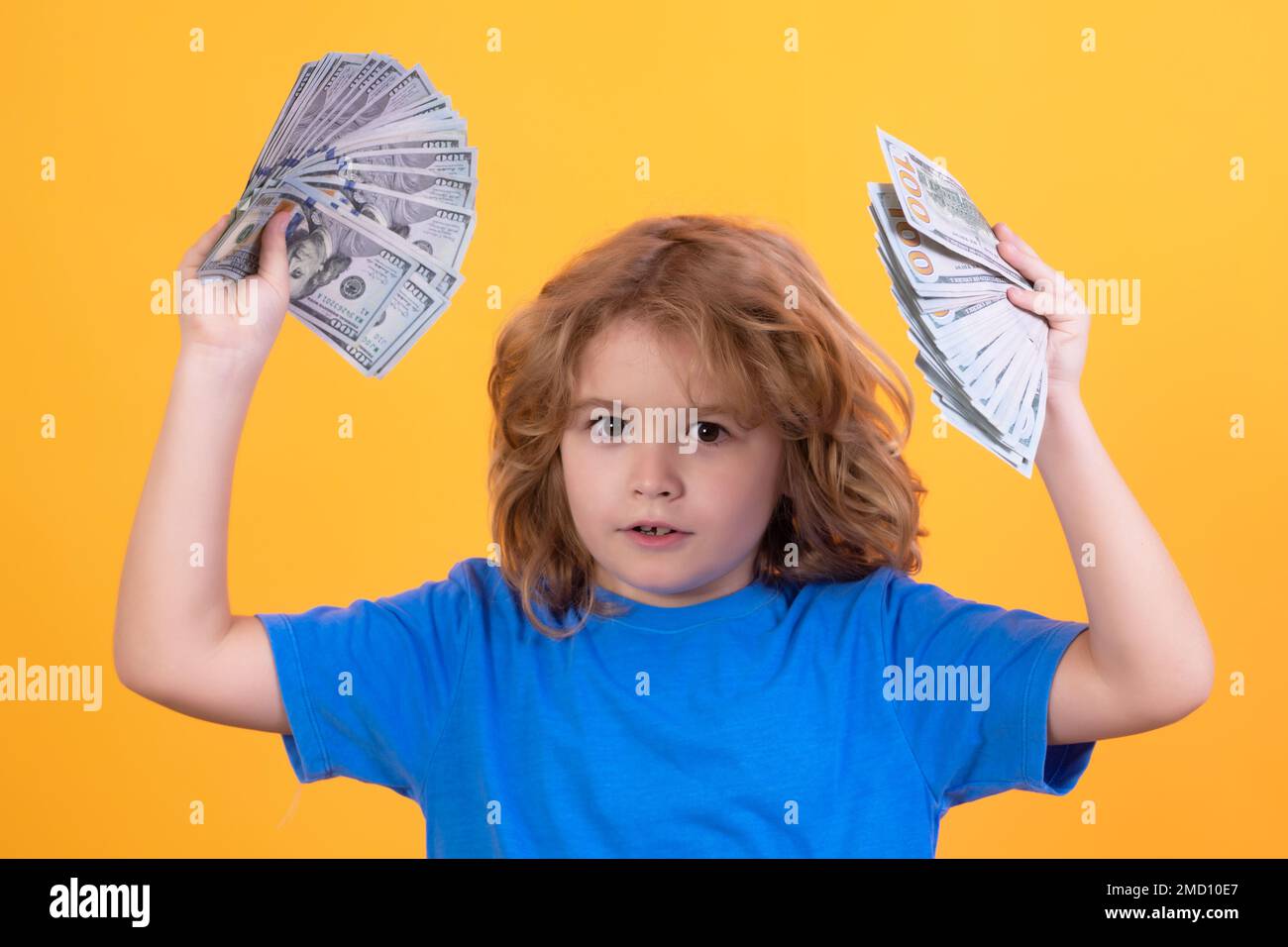 Enfant montrant des billets d'argent en dollars, se tenant rêveur de riche sur un arrière-plan isolé de studio. Banque D'Images