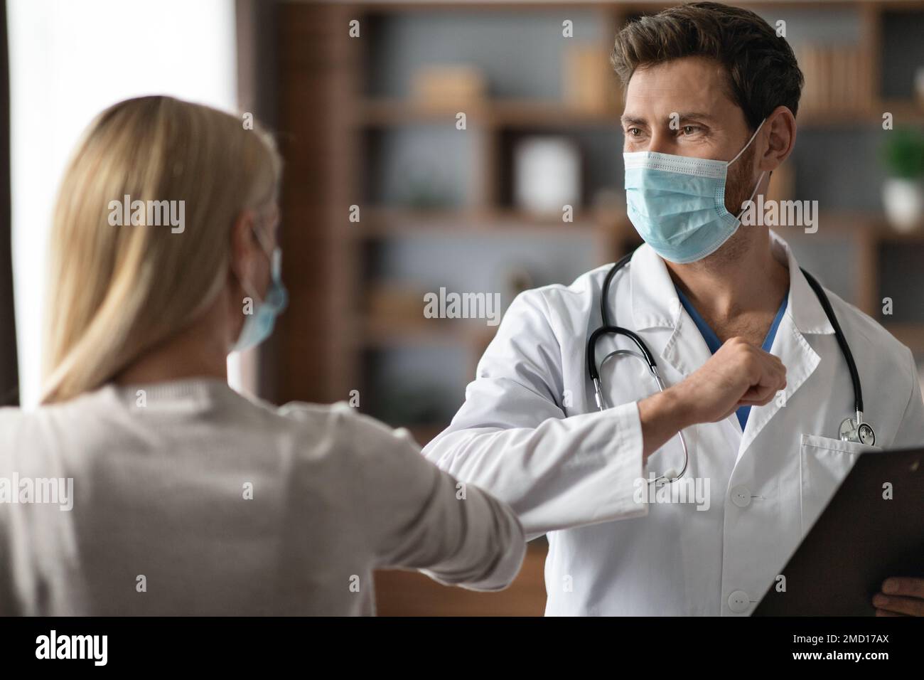 Un médecin de sexe masculin dans un masque médical qui rend le message d'accueil de la bosse du coude avec un patient de sexe féminin Banque D'Images