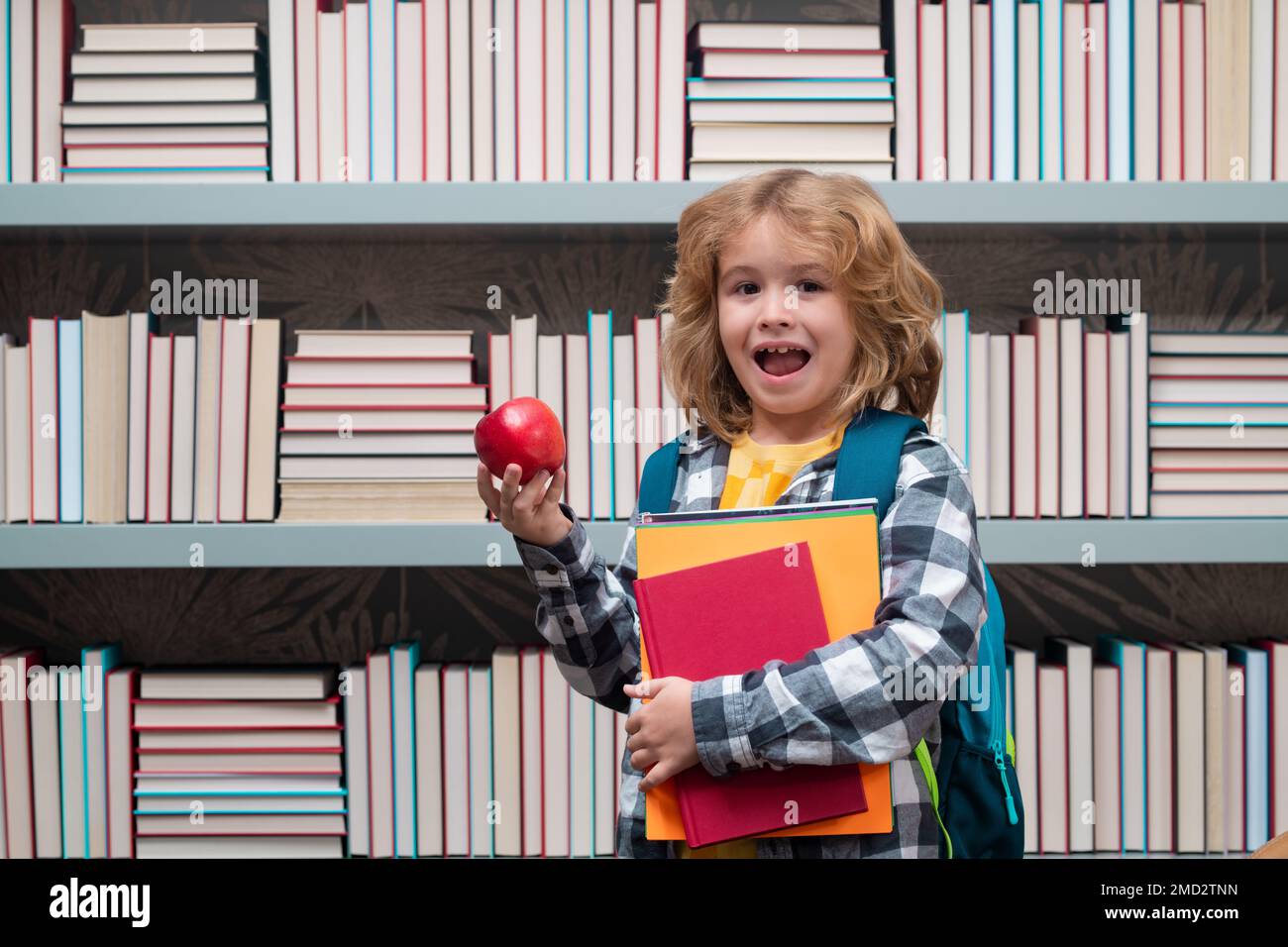 Garçon d'école avec des livres et de la pomme dans la bibliothèque. École enfant de 7-8 ans avec livre retourner à l'école. Petit étudiant. Banque D'Images