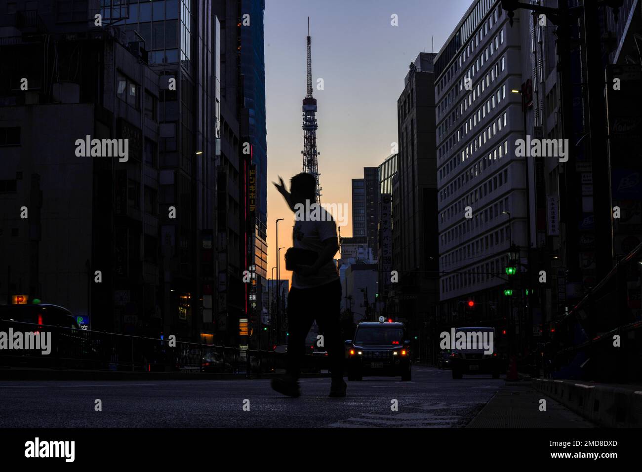 A man hails a taxi in Roppingi neighborhood, an entertainment district, in Tokyo Wednesday, Oct. 20, 2021, as Tokyo Tower is silhouetted against the sunrise colored sky in the background. Daily new COVID-19 cases have plummeted from a mid-August peak of nearly 6,000 in Tokyo, with caseloads in the densely populated capital now routinely below 100, an 11-month low. (AP Photo/Kiichiro Sato) Banque D'Images