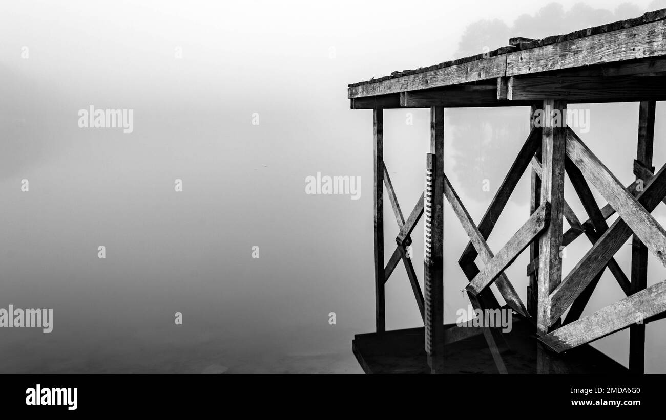 Un quai en bois s'étend sur un lac calme avec du brouillard. Banque D'Images