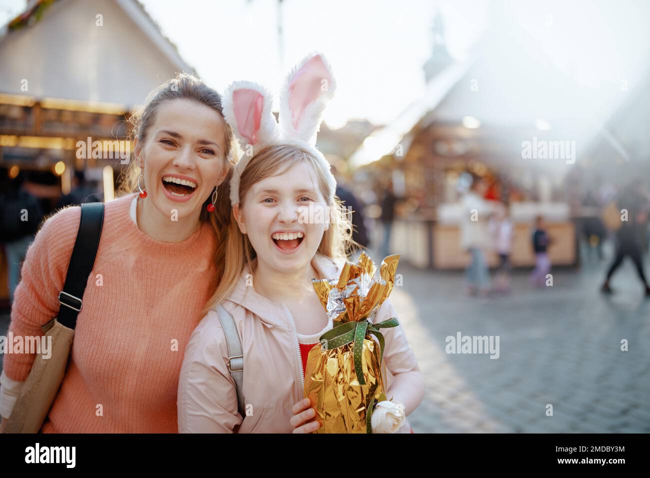 Pâques amusant. Portrait de la mère et de l'enfant modernes souriants avec l'oeuf de pâques doré à la foire dans la ville. Banque D'Images