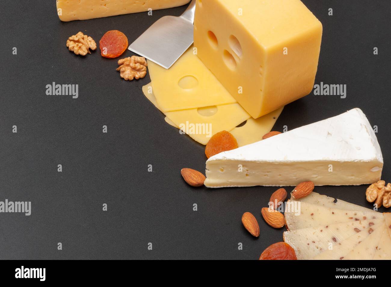 Différents types de fromage sur une planche en bois décorée de raisins, d'abricots secs et de noix Banque D'Images