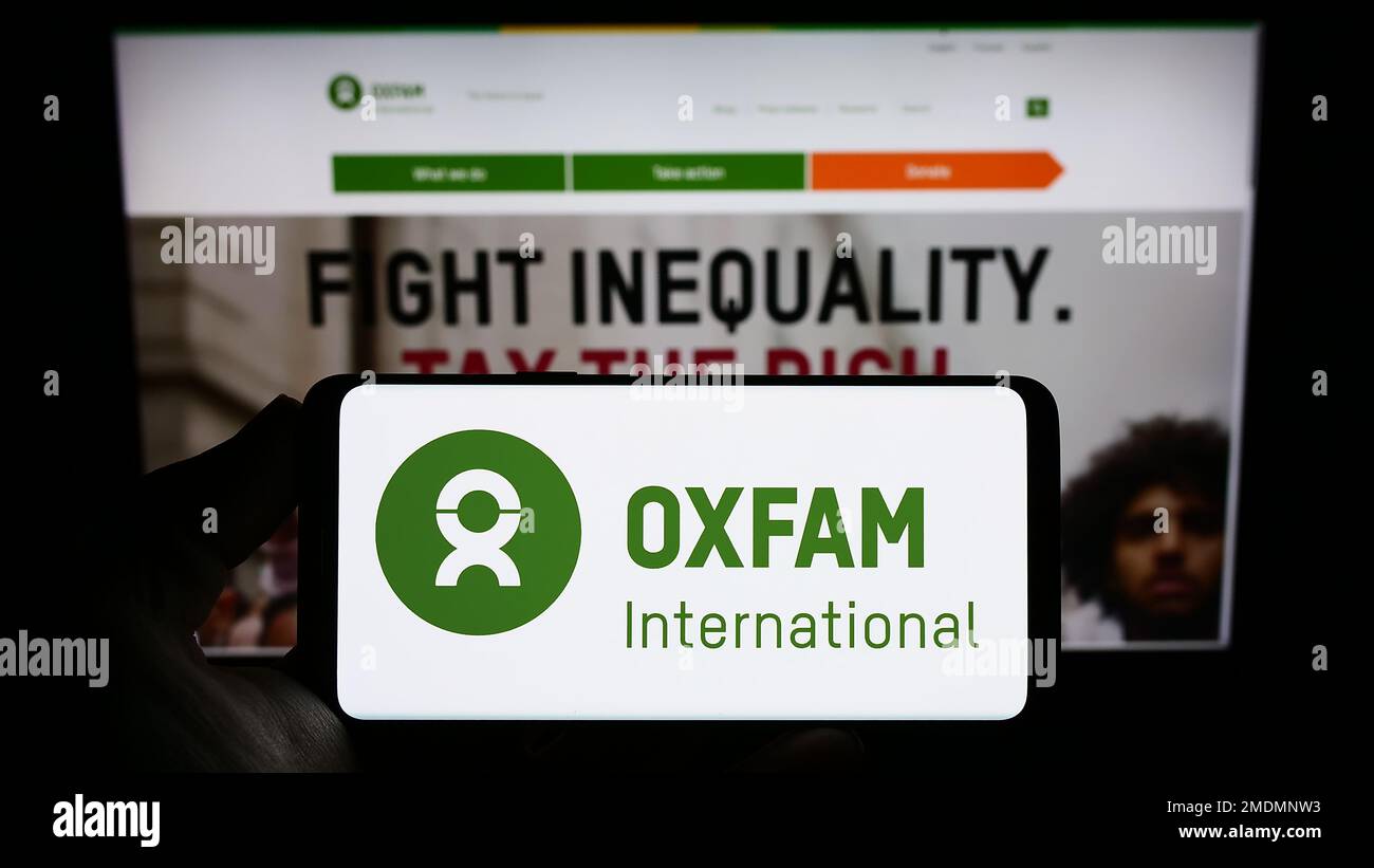 Personne tenant un smartphone avec le logo de la confédération Oxfam International à l'écran devant le site Web. Mise au point sur l'affichage du téléphone. Banque D'Images