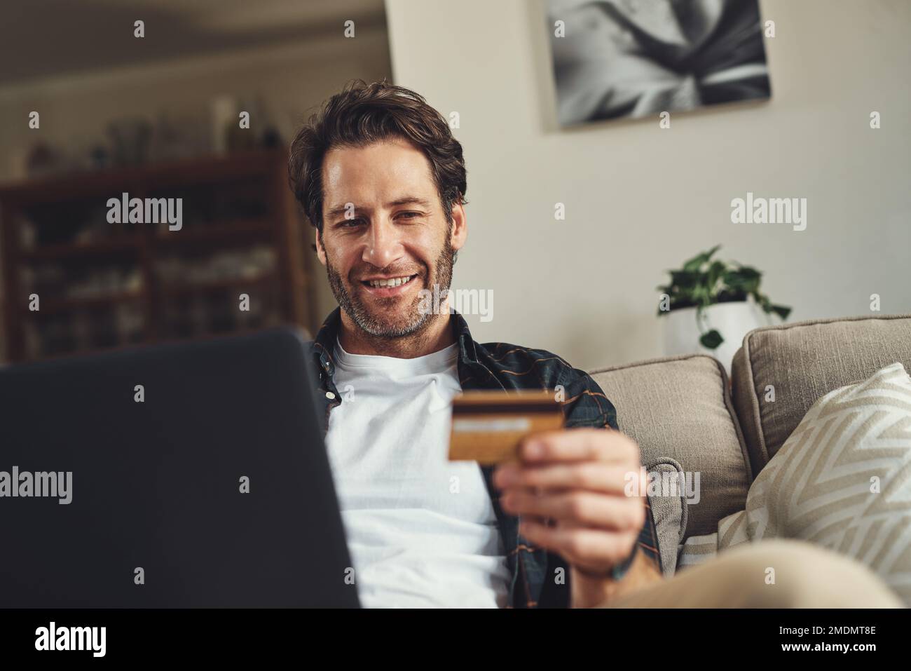 Il est temps de dépenser. un beau jeune homme utilisant son ordinateur portable et sa carte de crédit tout en se relaxant sur un canapé à la maison. Banque D'Images