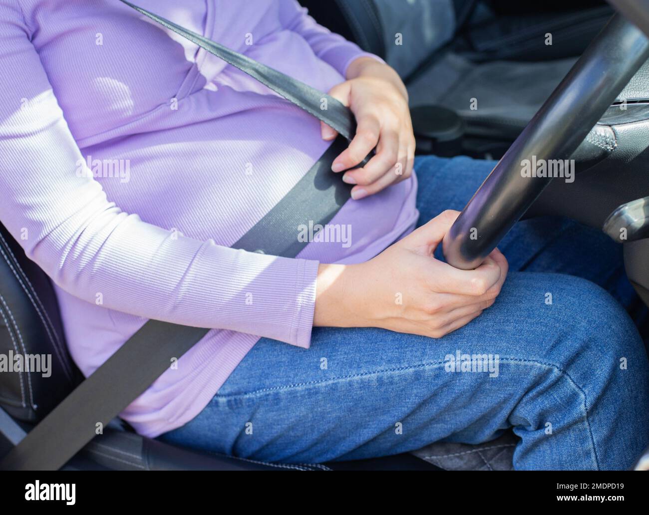 Une femme enceinte portant une ceinture de sécurité conduit une