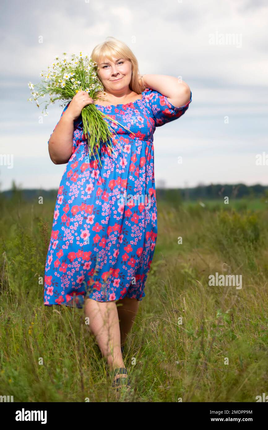 Belle femme de taille plus avec des cheveux blancs dans une robe d'été posant à l'extérieur avec des pâquerettes. Fille de chubby dans un pré avec des fleurs. Banque D'Images
