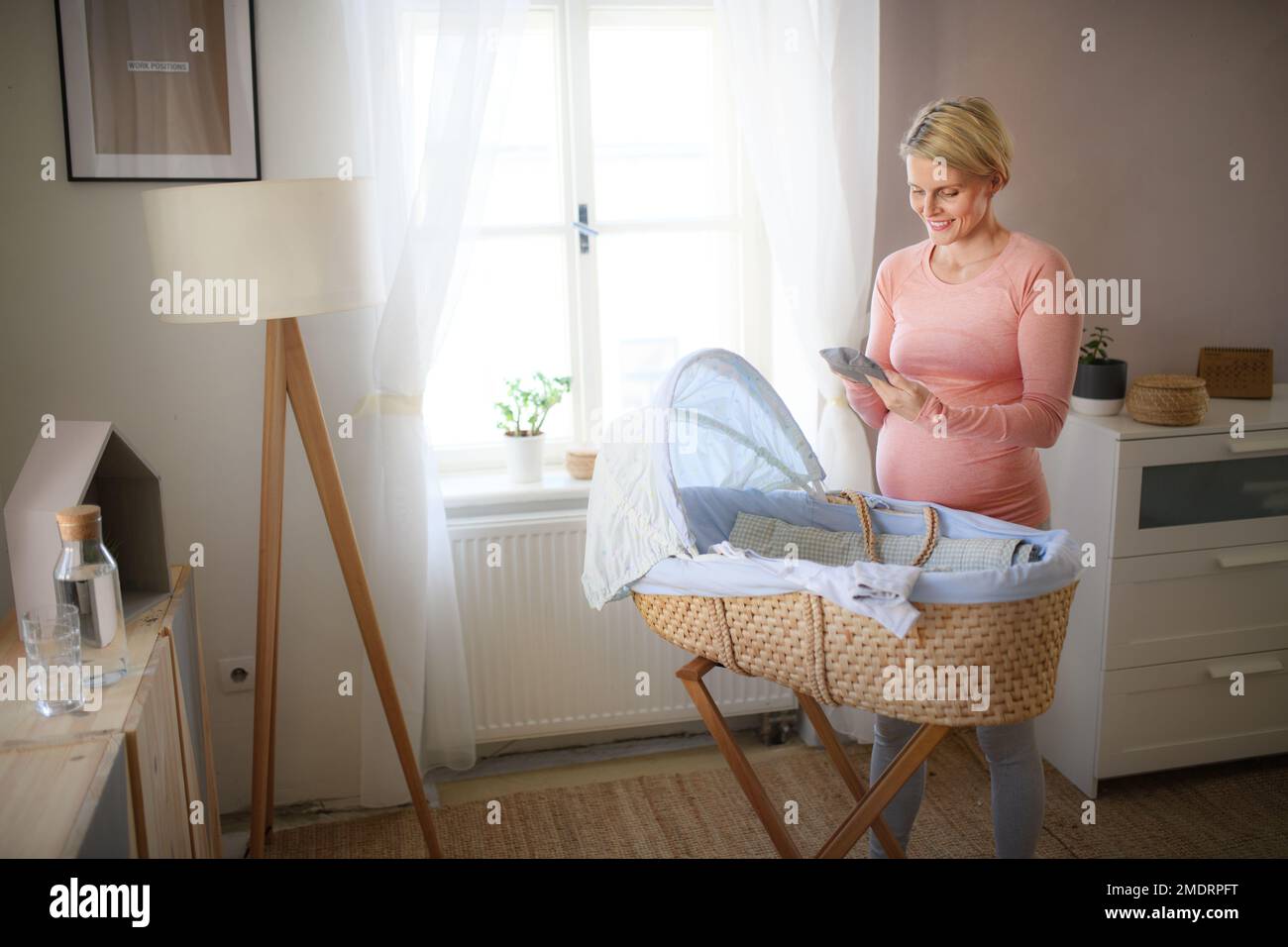 Bonne femme enceinte regardant de petits vêtements pour son bébé. Banque D'Images