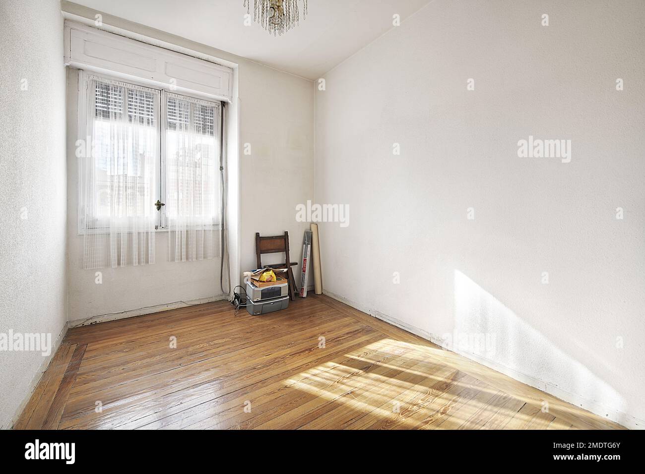 chambre vide d'une maison avec un plancher de beau parquet de pin avec une fenêtre avec des rideaux blancs et quelques objets anciens dans le coin Banque D'Images