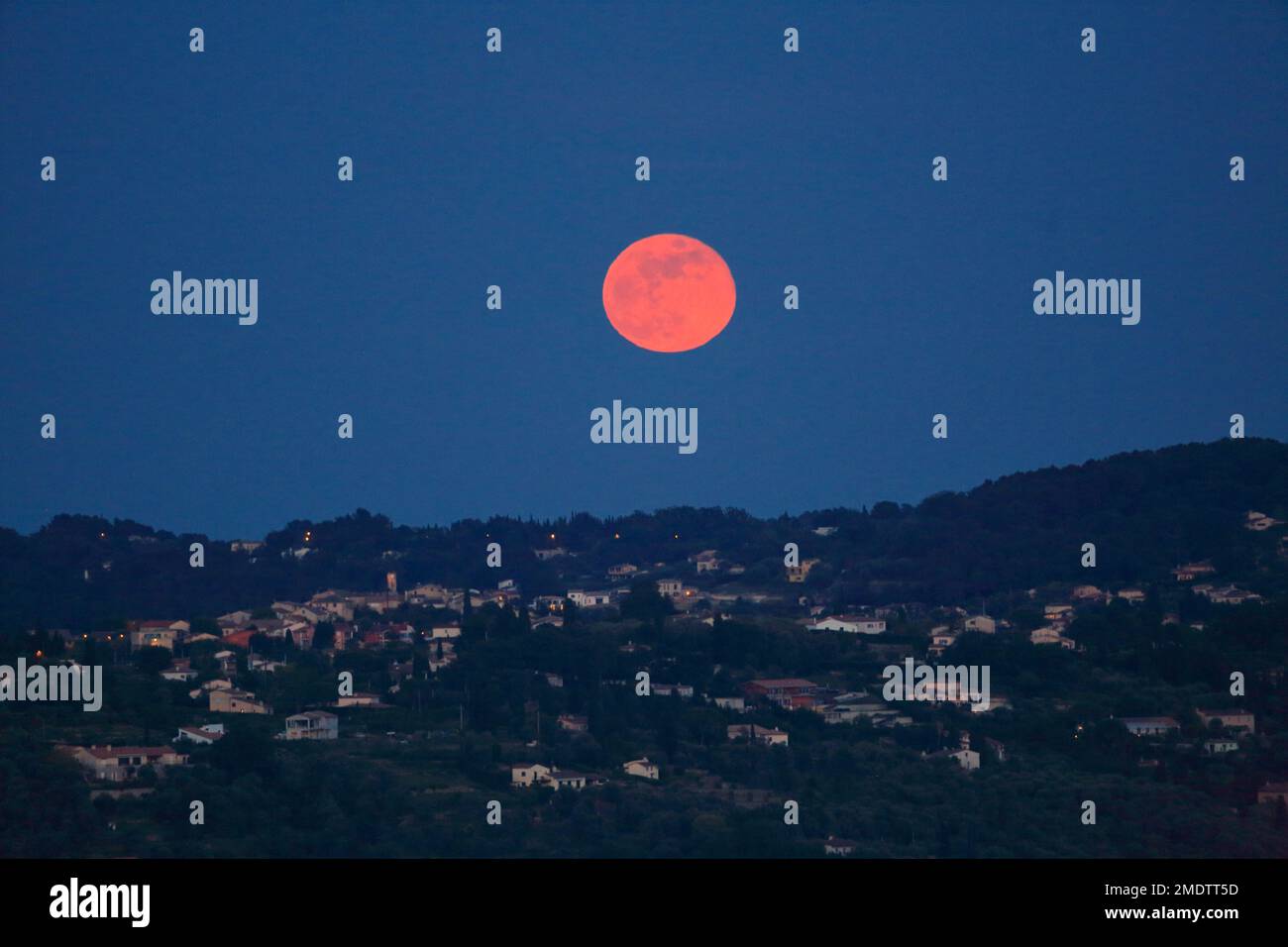 Pleine lune rouge au-dessus du village de Plascassier, Alpes Maritimes, Côte d'Azur. Banque D'Images
