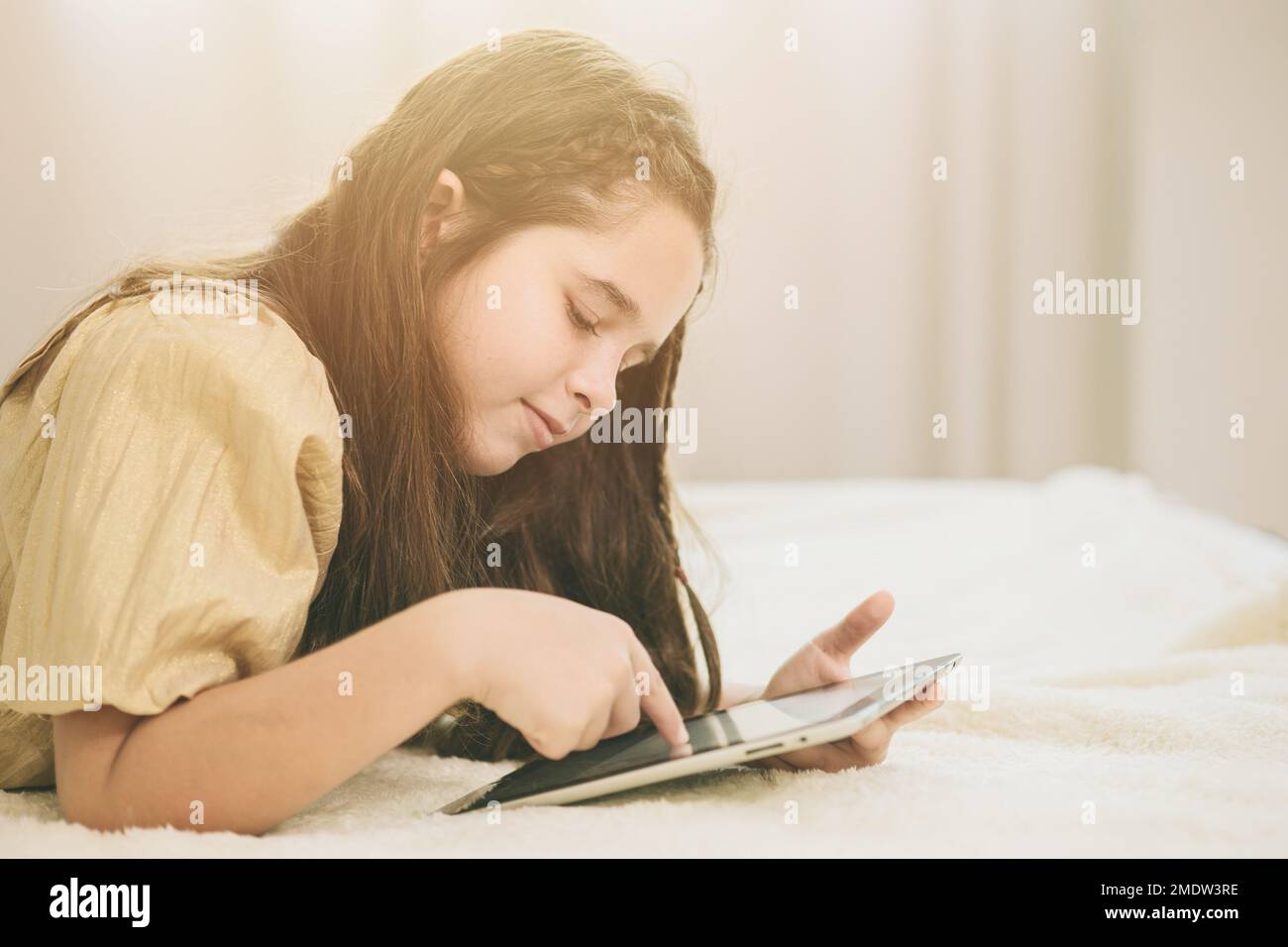 enfant posé sur le lit à l'aide d'une tablette pour l'auto-apprentissage à la maison. adorable fille joue à des jeux de vacances sur un écran tactile. Banque D'Images